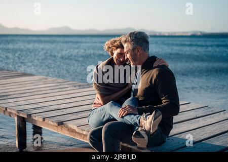 Glückliches reifes Paar, das auf dem Steg sitzt Stockfoto