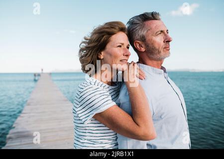 Lächelnde reife Frau mit Händen auf der Schulter des Mannes am Steg Stockfoto