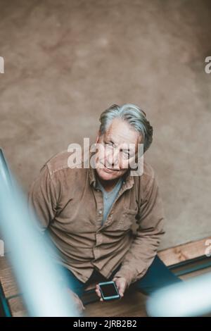 Älterer Mann mit Mobiltelefon sitzt Stockfoto