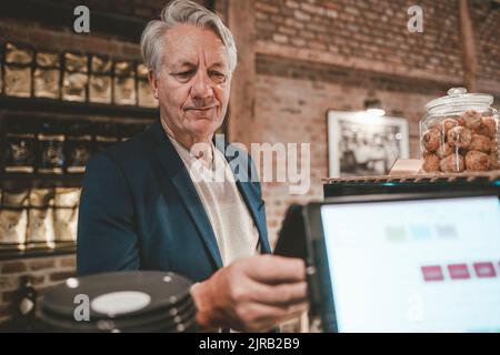 Leitender Geschäftsmann, der am Cafe-Schalter per Smartphone bezahlt Stockfoto