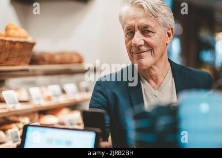 Lächelnder Geschäftsmann, der am Cafe-Schalter per Smartphone bezahlt Stockfoto