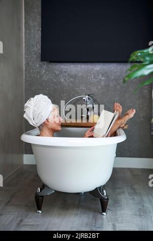 Reife Frau, die zu Hause in der Badewanne ein Buch liest Stockfoto