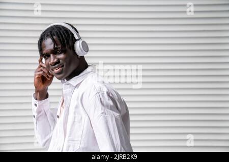 Lächelnder junger Mann, der über kabellose Kopfhörer Musik hört Stockfoto