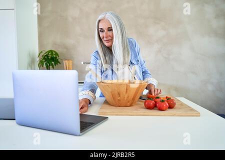 Frau mit Tomaten mit Laptop in der Küche Stockfoto