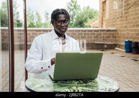 Junge Freiberuflerin, die eine Brille trägt und am Laptop im Straßencafé arbeitet Stockfoto