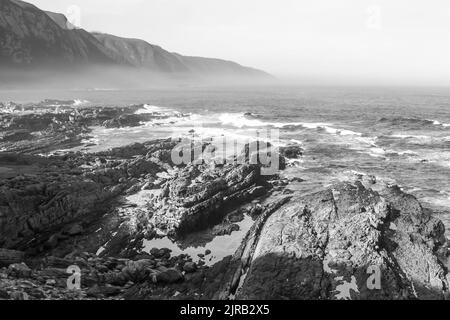 Schwarz-Weiß-Ansicht der verdrehten Felsen der zerklüfteten und steilen Küste von Tsitikamma, Südafrika. Stockfoto