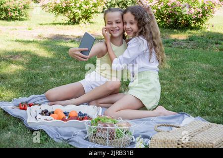 Mädchen zieht die Wange der Schwester, die Selfie im Park nimmt Stockfoto