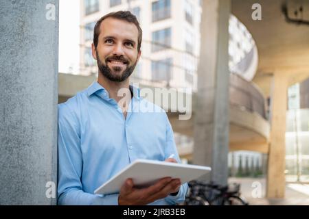 Glücklicher junger Geschäftsmann mit Tablet-PC, der unter der Brücke steht Stockfoto