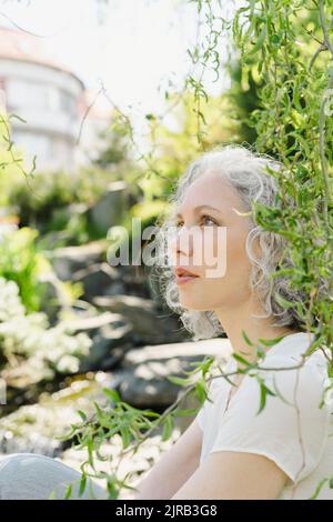 Kontemplative Frau, die im Park bei Pflanzen sitzt Stockfoto