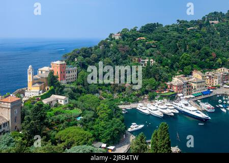 Chiesa San Giorgio, grüne Hügel und Luxusboote, die in der winzigen Hafenstadt Portofino, Ligurien, Italien, festgemacht sind Stockfoto