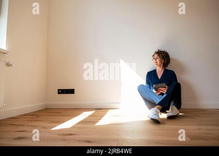 Lächelnder Immobilienmakler mit Tablet-PC, der zu Hause auf dem Boden sitzt Stockfoto