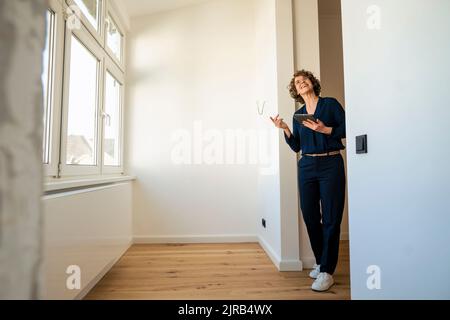 Lächelnder Immobilienmakler mit Tablet-PC, der vor der Tür steht Stockfoto