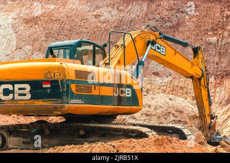 Ein JCB-Bulldozer/Baggerlader/Planierschild/Raupenfahrzeug, der große Mengen Sand aushubt, während er in Indien Straßenbauarbeiten durchführt. Stockfoto