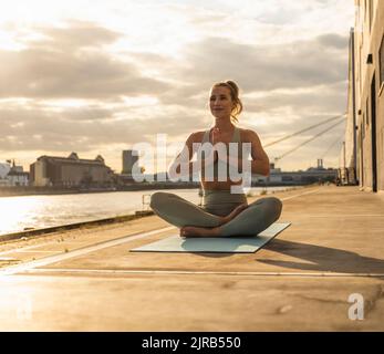 Lächelnde junge Frau mit den Händen, die Yoga auf der Promenade machten Stockfoto