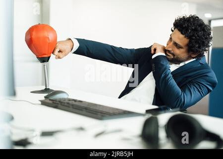 Entschlossener Geschäftsmann, der Speed Bag am Schreibtisch im Büro boxte Stockfoto