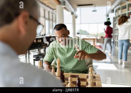 Glücklicher Geschäftsmann, der mit einem Kollegen im Büro Schach spielt Stockfoto