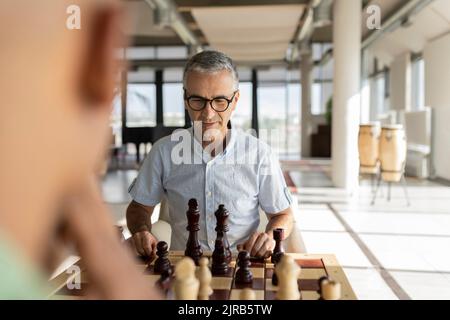 Reifer Geschäftsmann, der mit einem Kollegen im Büro Schach spielt Stockfoto