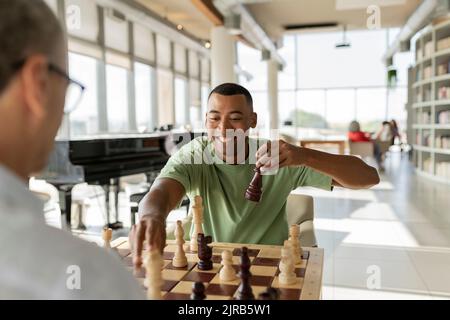Glücklicher Geschäftsmann, der mit einem Kollegen im Büro ein Schachspiel abholt und ein Brettspiel spielt Stockfoto