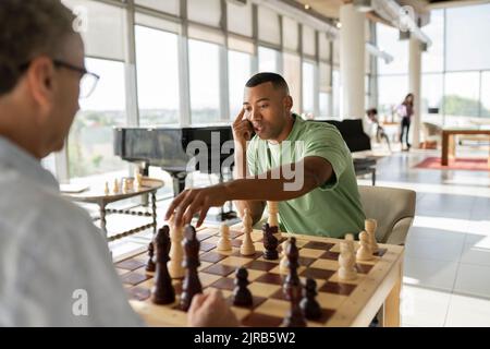 Geschäftsmann, der mit einem Kollegen im Büro ein Schachspiel abholt und ein Brettspiel spielt Stockfoto