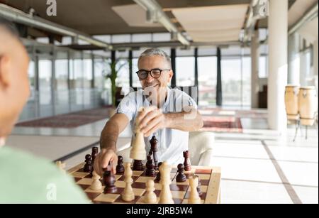 Lächelnder Geschäftsmann mit Brillen, der mit einem Kollegen im Büro Schach spielt Stockfoto