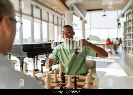 Lächelnder Geschäftsmann, der mit einem reifen Kollegen im Büro Schach spielt Stockfoto
