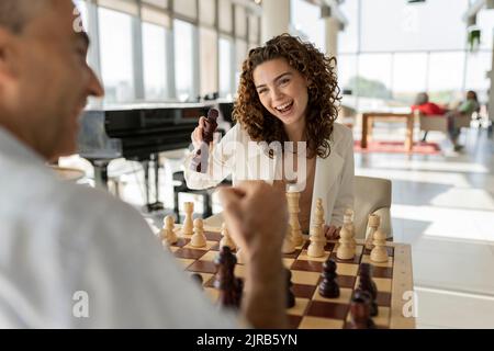 Glückliche junge Geschäftsfrau, die mit einem reifen Kollegen im Amt Schach spielt Stockfoto