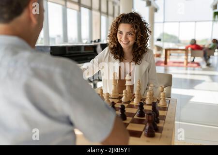 Lächelnde junge Geschäftsfrau, die mit einem Kollegen im Büro Schach spielt Stockfoto