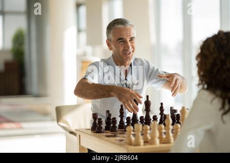 Lächelnder Geschäftsmann im Gespräch mit einem Kollegen, der im Büro Schach spielt Stockfoto