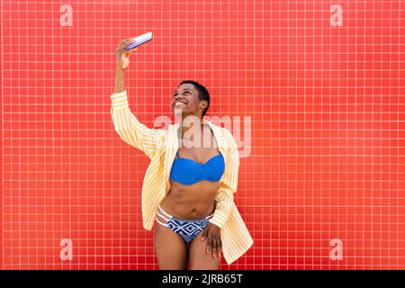 Fröhliche Frau im Bikini, die Selfie über das Mobiltelefon nimmt Stockfoto