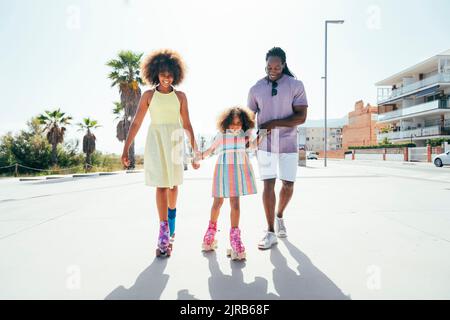 Lächelnde Töchter Rollschuh mit Vater an sonnigen Tag Stockfoto