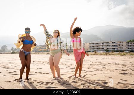 Unbeschwerte multirassische Freunde, die an sonnigen Tagen am Strand tanzen Stockfoto