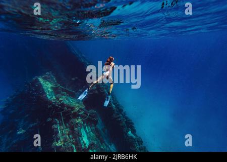 Frau schwimmt unter Wasser durch ein Schiffswrack im Meer Stockfoto