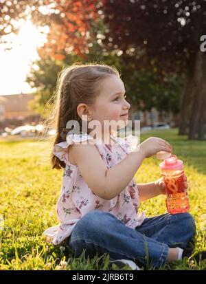 Nettes Mädchen tauche Blase Zauberstab in Flasche im Park Stockfoto