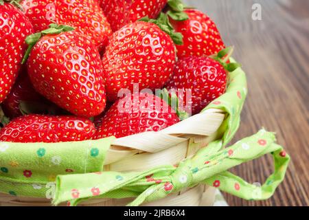 Frische reife Erdbeeren im Korb auf braunem Holzhintergrund Stockfoto