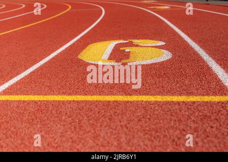 Nahaufnahme der Fahrspur 6 auf einer neuen roten Laufstrecke mit weißen Linien und anderen Markierungen. Stockfoto