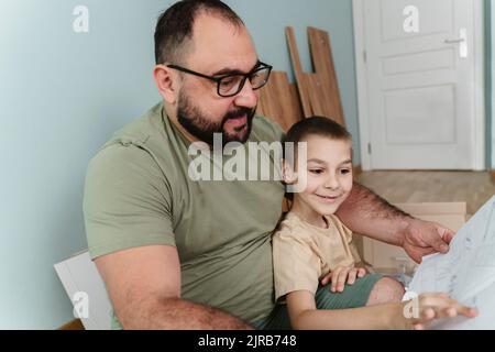 Lächelnder Mann mit Sohn, der zuhause die Bedienungsanleitung liest Stockfoto