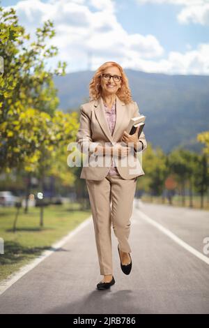 Porträt einer Frau, die Bücher hält und auf einer Fußgängerstraße läuft Stockfoto