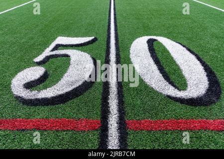 Kunstrasen Fußball 50 Yard Linie in weiß mit schwarzen Zahlen Schatten zusammen mit roten Lacrosse Linie und gelben Fußball Mitte Feldlinie Stockfoto