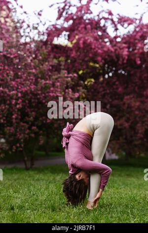 Frau, die Uttanasana vor Apfelblütenbäumen praktiziert Stockfoto