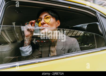 Geschäftsfrau mit Sonnenbrille und Blick vom Taxifenster Stockfoto