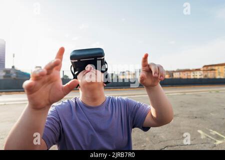 Teenager-Junge trägt Virtual-Reality-Simulator gestikulieren auf dem Fußweg Stockfoto