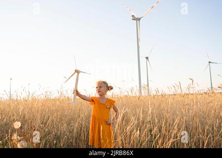 Mädchen mit Windturbinenmodell, das im Weizenfeld steht Stockfoto