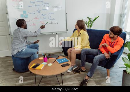 Geschäftsmann zeigt auf Whiteboard und diskutiert mit Kollegen im Büro Stockfoto