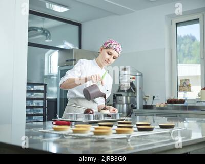 Junger Konditor gießt Schokoladensirup auf das Dessert Stockfoto