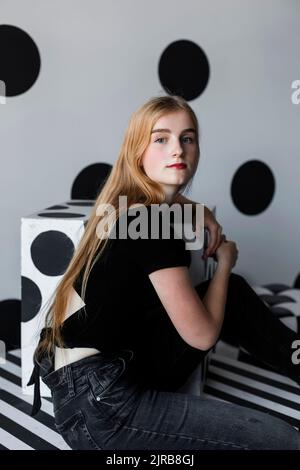 Schönes Teenager-Mädchen, das vor einer gepunkteten Wand sitzt Stockfoto