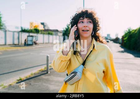 Junge Frau, die auf der Straße mit dem Handy spricht Stockfoto