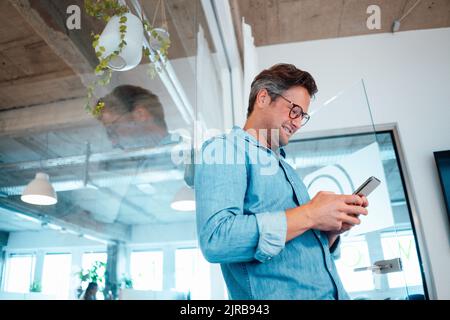 Lächelnde Geschäftsmann mit Smartphone im Büro Stockfoto