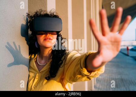 Junge Frau mit VR-Brille tut Stop-Geste von Spalte Stockfoto