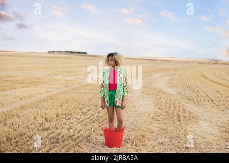 Junge Frau, die im Eimer auf dem Feld steht Stockfoto