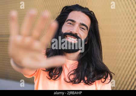 Lächelnder bärtiger Mann mit langen Haaren und gestikulierenden Händen Stockfoto